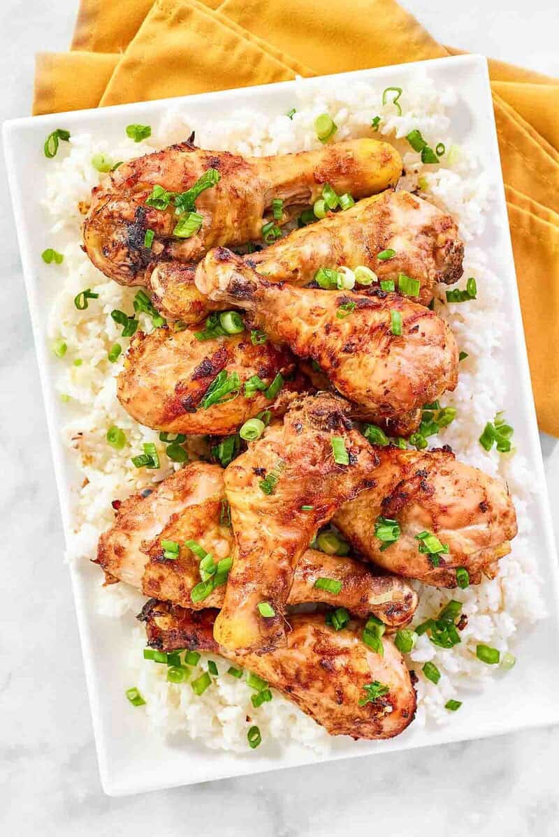 Baked chicken drumsticks with miso glaze served over rice and garnished with green onions.