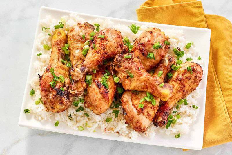 A platter of baked chicken drumsticks with glaze over rice.