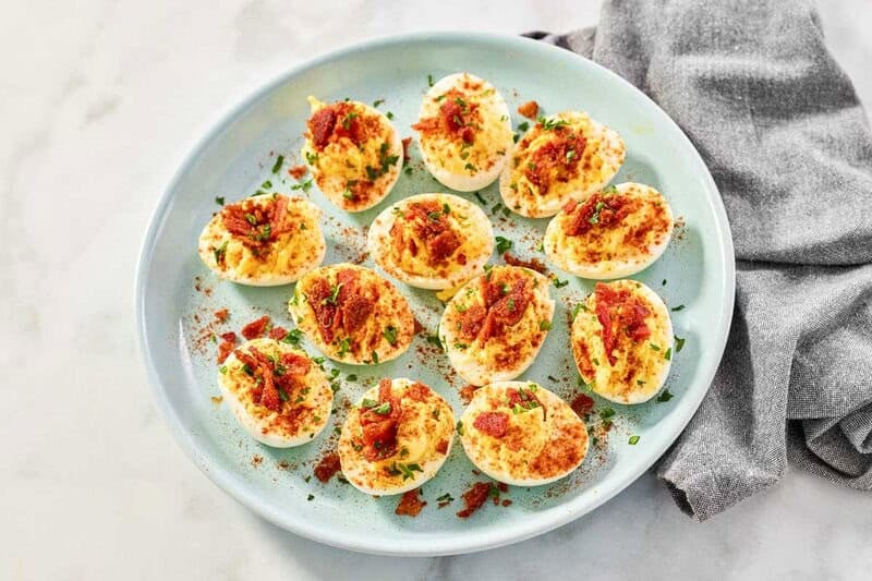 Deviled eggs with brown sugar candied bacon bits arranged on a platter.