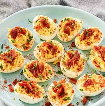 Deviled eggs topped with candied bacon bits and paprika.
