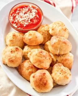 Cheesy garlic bread balls served with marinara on a platter.