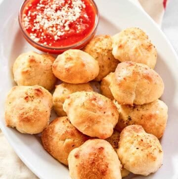 Cheesy garlic bread balls served with marinara on a platter.