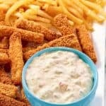 A platter of crispy fish sticks and fries served with tartar sauce.