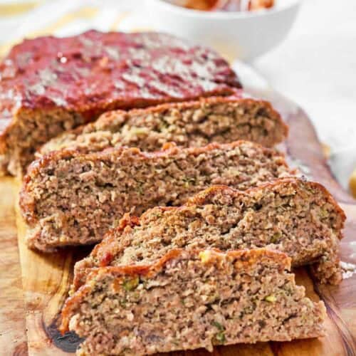 A meatloaf with a rich glaze sliced on a wood cutting board.
