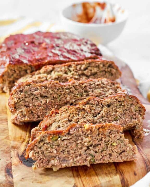 A meatloaf with a rich glaze sliced on a wood cutting board.