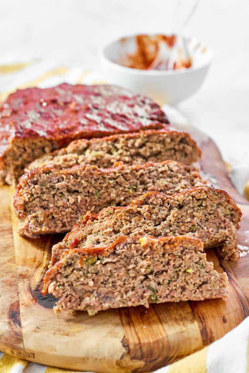 A meatloaf with a rich glaze sliced on a wood cutting board.