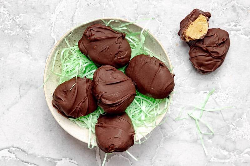Peanut butter eggs with chocolate coating on a plate with Easter basket straw.
