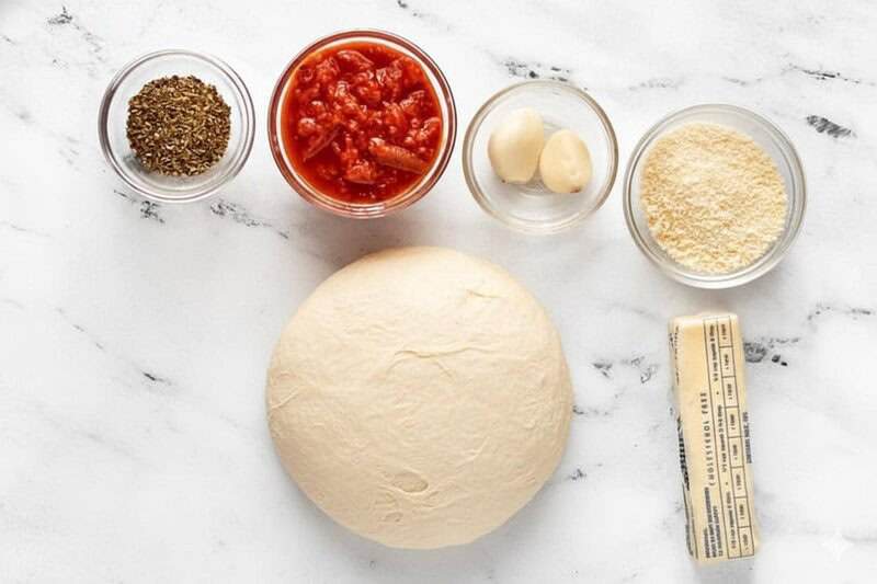 pizza dough, oregano, pizza sauce, fresh garlic, cheese, and margarine on a marble board