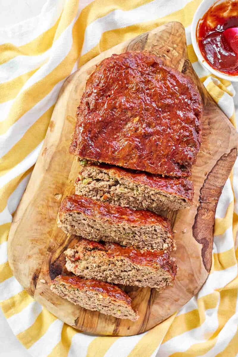 A meatloaf with glaze partially sliced on a wood cutting board.