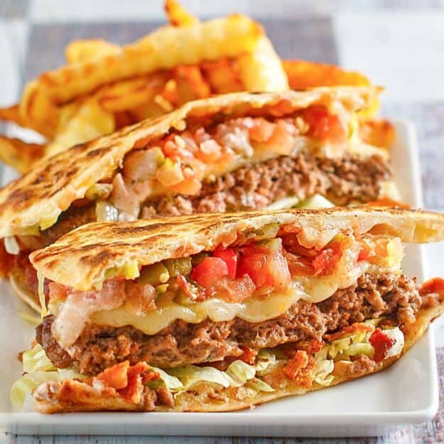 Closeup of a quesadilla burger on a white plate.