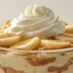 Banana pudding in a glass bowl topped with whipped cream.