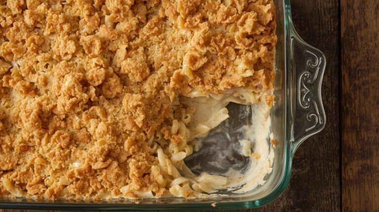 Tuna noodle casserole with egg noodles and crispy cracker topping in a vintage glass baking dish on a rustic table.