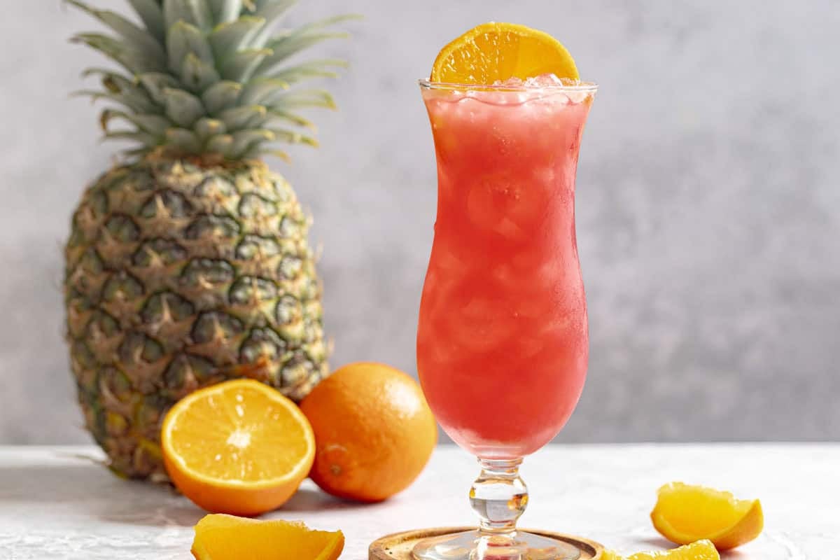 Armadillo rum punch in a hurricane glass, a pineapple, and oranges.