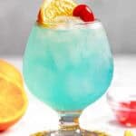 A blue curacao, rum, and lemonade cocktail garnished with an orange slice and a marschino cherry.