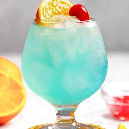 A blue curacao, rum, and lemonade cocktail garnished with an orange slice and a marschino cherry.