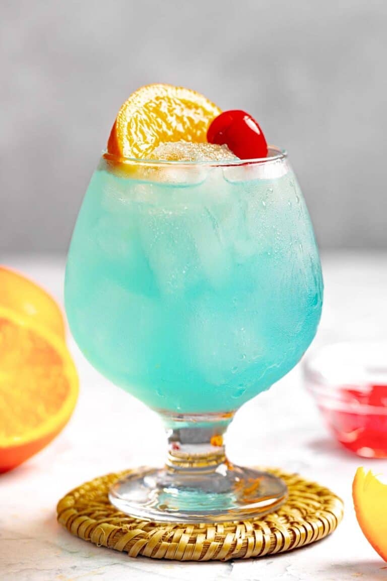 A blue curacao, rum, and lemonade cocktail garnished with an orange slice and a marschino cherry.