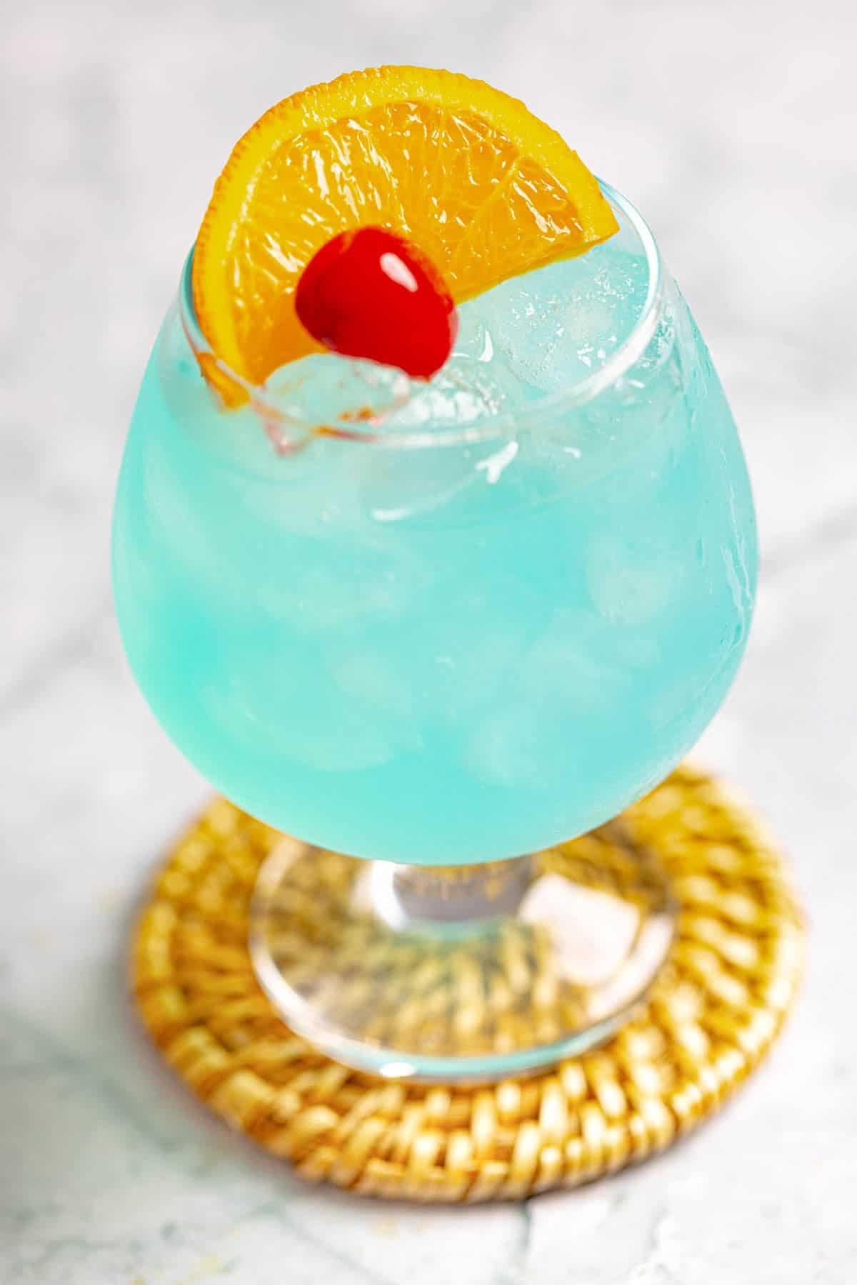 A blue curacao lemonade cocktail garnished with a lemon slice and cherry.