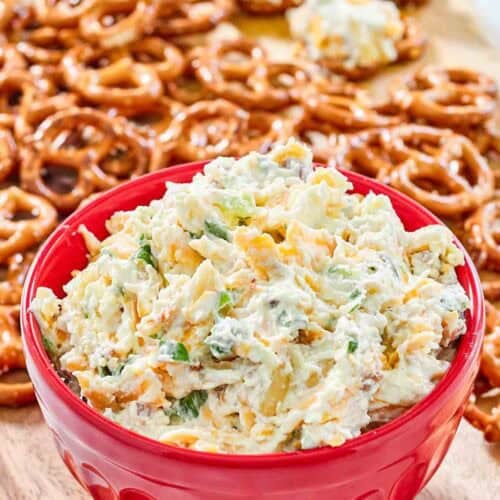 A bowl of creamy cheddar bacon dip served with mini pretzels.