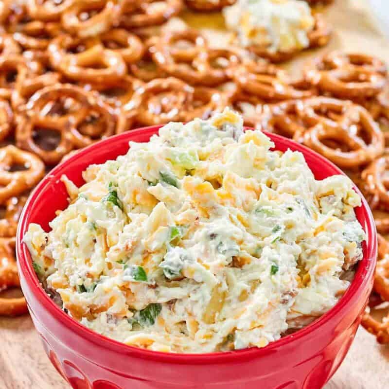 A bowl of creamy cheddar bacon dip served with mini pretzels.