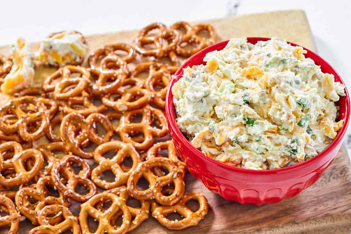 A bowl of creamy and cheese bacon dip served with mini pretzels.