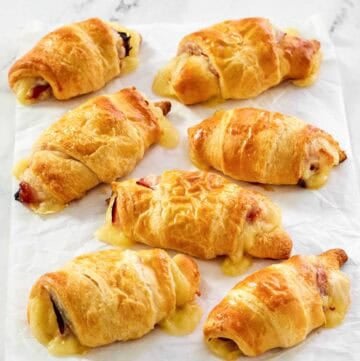 Flaky ham and Swiss cheese rolls on parchment paper.