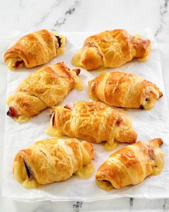 Flaky ham and Swiss cheese rolls on parchment paper.