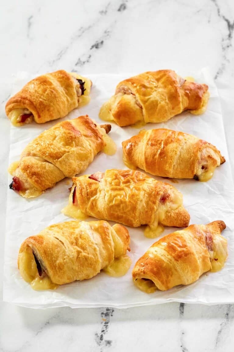 Flaky ham and Swiss cheese rolls on parchment paper.
