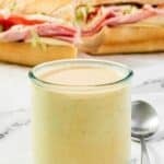 A jar of spicy hot ranch dressing and an Italian sub sandwich behind it.