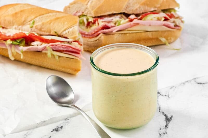 An Italian sub sandwich and a jar of spicy ranch sauce.