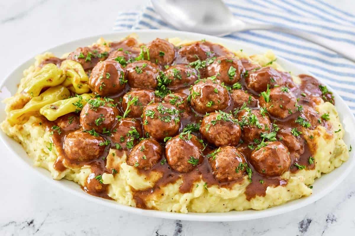 Slow cooker pepperoncini meatballs with gravy served over mashed potatoes.