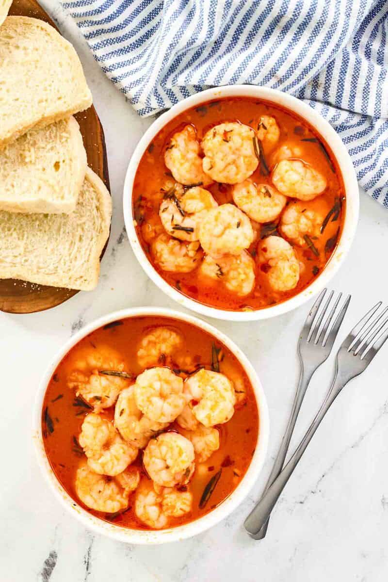 Bowls of shrimp in tomato herb sauce with slices of bread nearby.