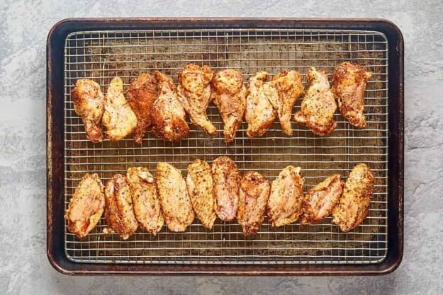 Smoked seasoned rubbed wings on a wire rack over a baking sheet.
