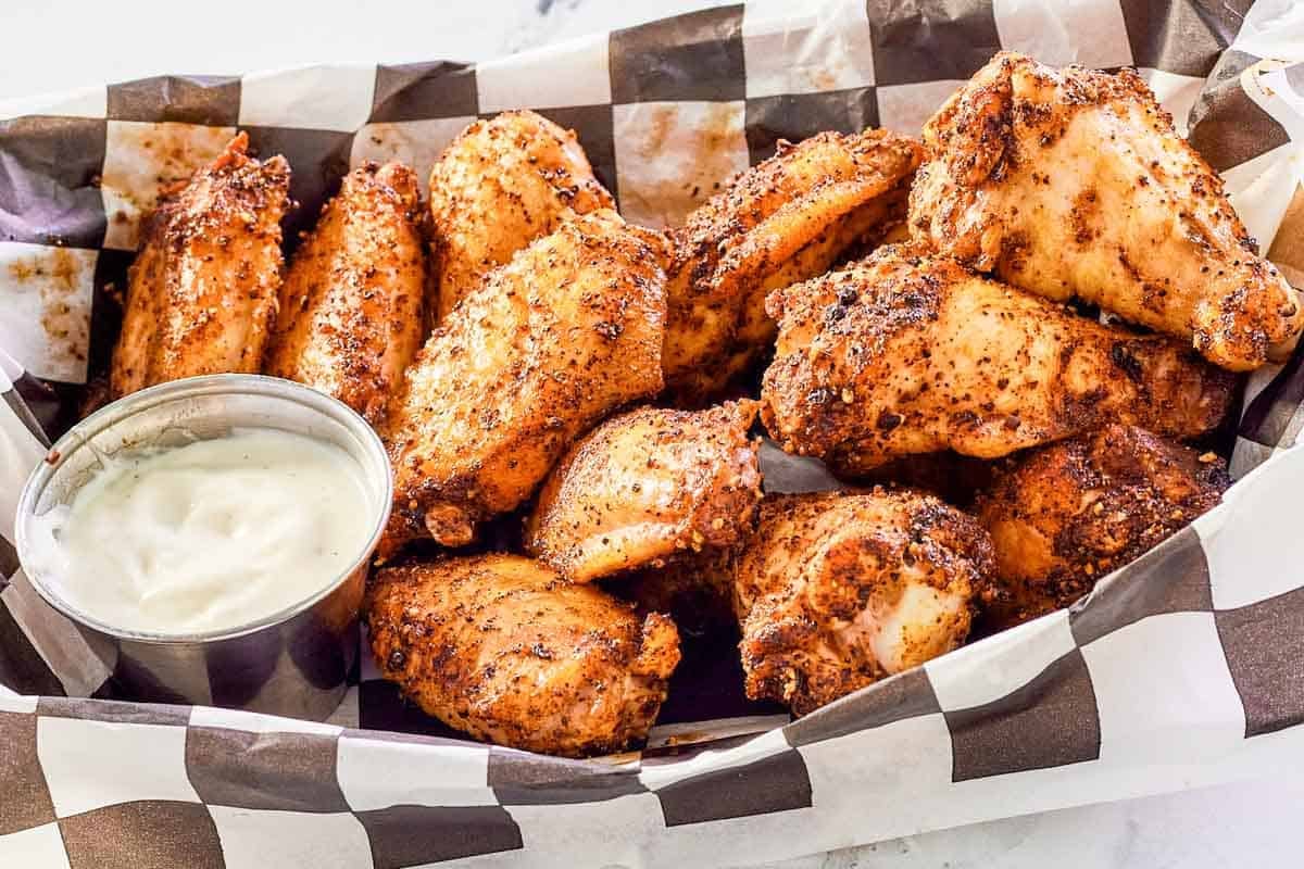 Smoked seasoned chicken wings and dipping sauce in a serving basket.