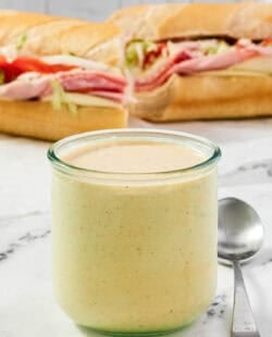 A jar of spicy ranch dressing and a sub sandwich behind it.