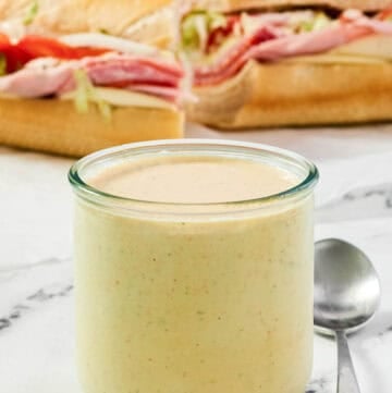 A jar of spicy ranch dressing and a sub sandwich behind it.