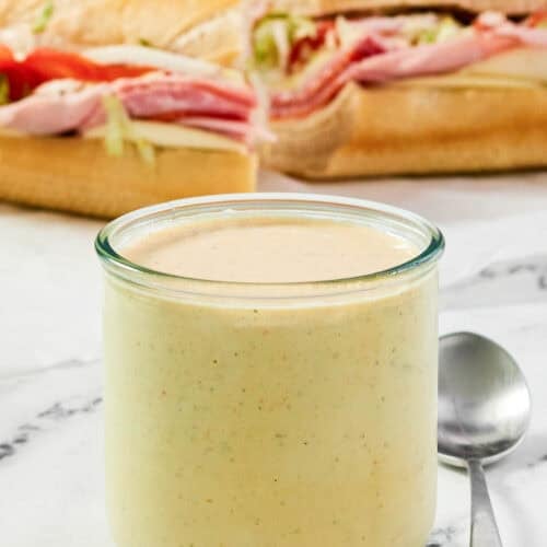 A jar of spicy ranch dressing and a sub sandwich behind it.
