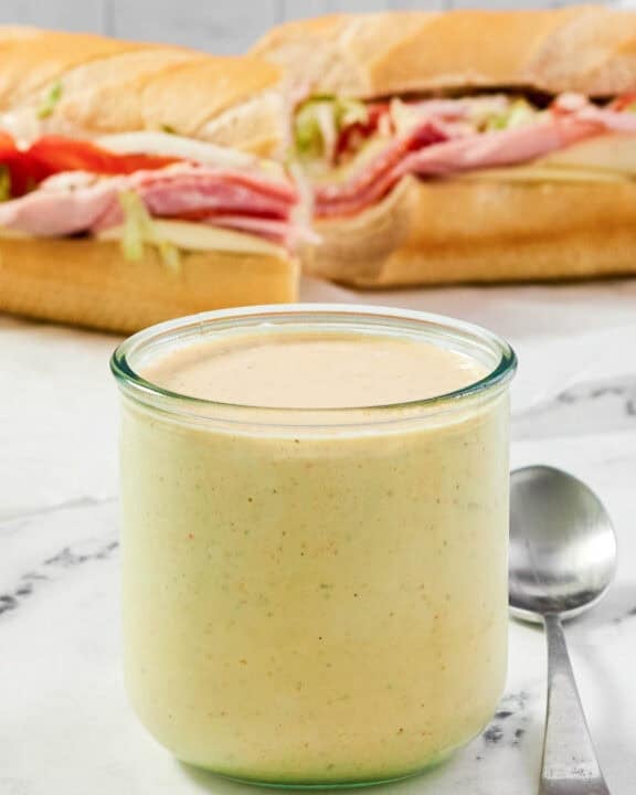 A jar of spicy ranch dressing and a sub sandwich behind it.