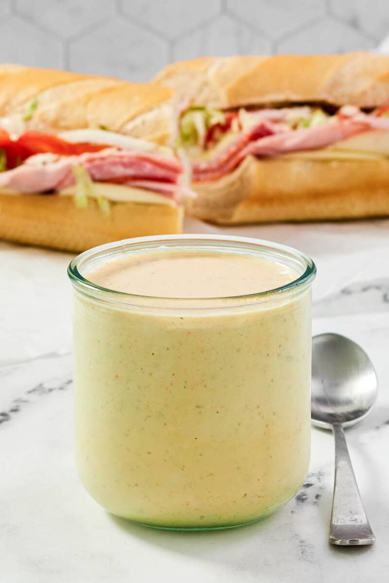 A jar of spicy ranch dressing and a sub sandwich behind it.