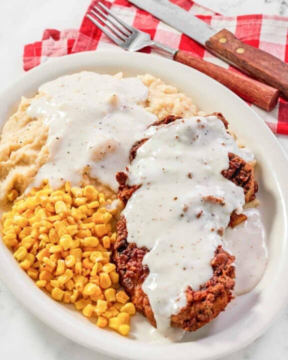 White gravy over chicken fried steak and mashed potatoes and corn on a plate.