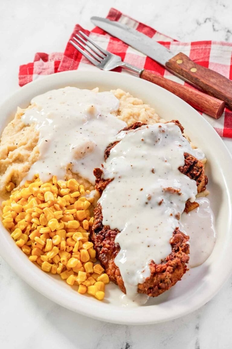 White gravy over chicken fried steak and mashed potatoes and corn on a plate.