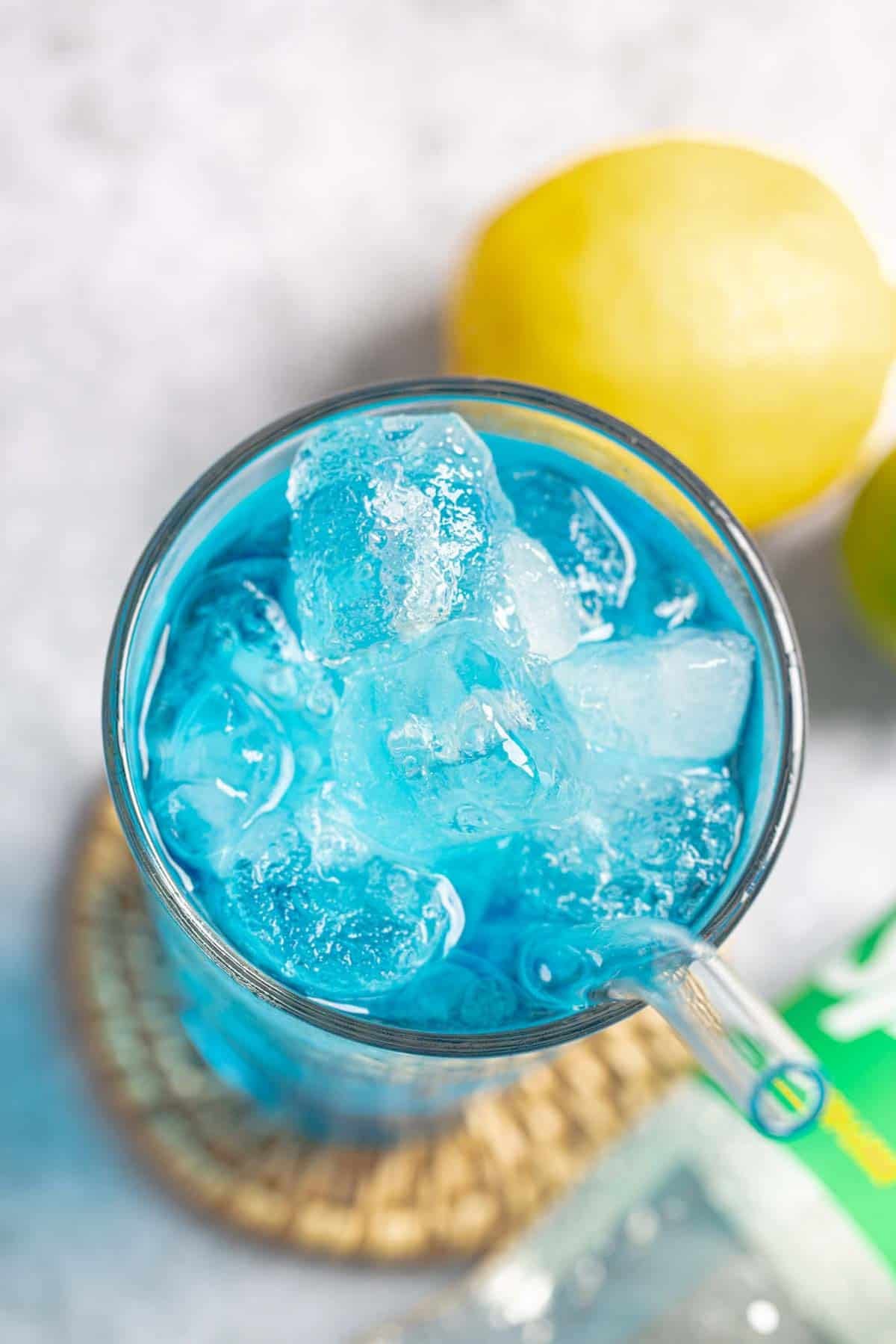 A blue lemon, lime, and coconut drink and a lemon next to it.