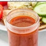 A jar of copycat CAVA hot harissa vinaigrette dressing and sliced veggies behind it.