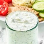 Creamy copycat CAVA tzatziki sauce in a jar and a salad behind it.