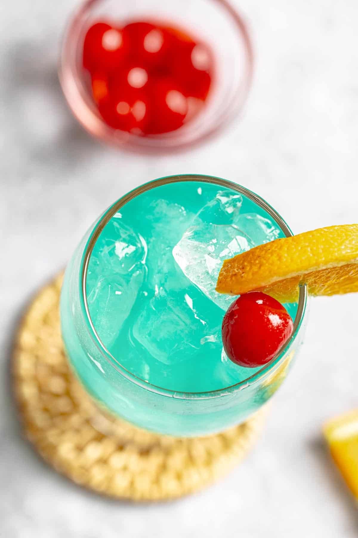 A coconut rum blue curacao drink garnished with a cherry and lemon slice.