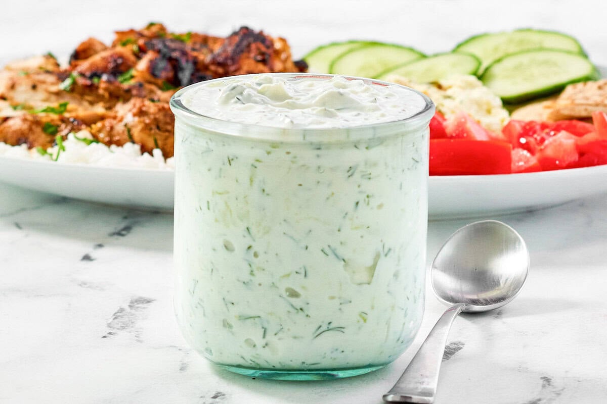 Creamy dill garlic yogurt sauce in a small jar and a grilled chicken salad behind it.