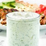 Creamy garlic dill yogurt sauce in a small jar in front of a salad.