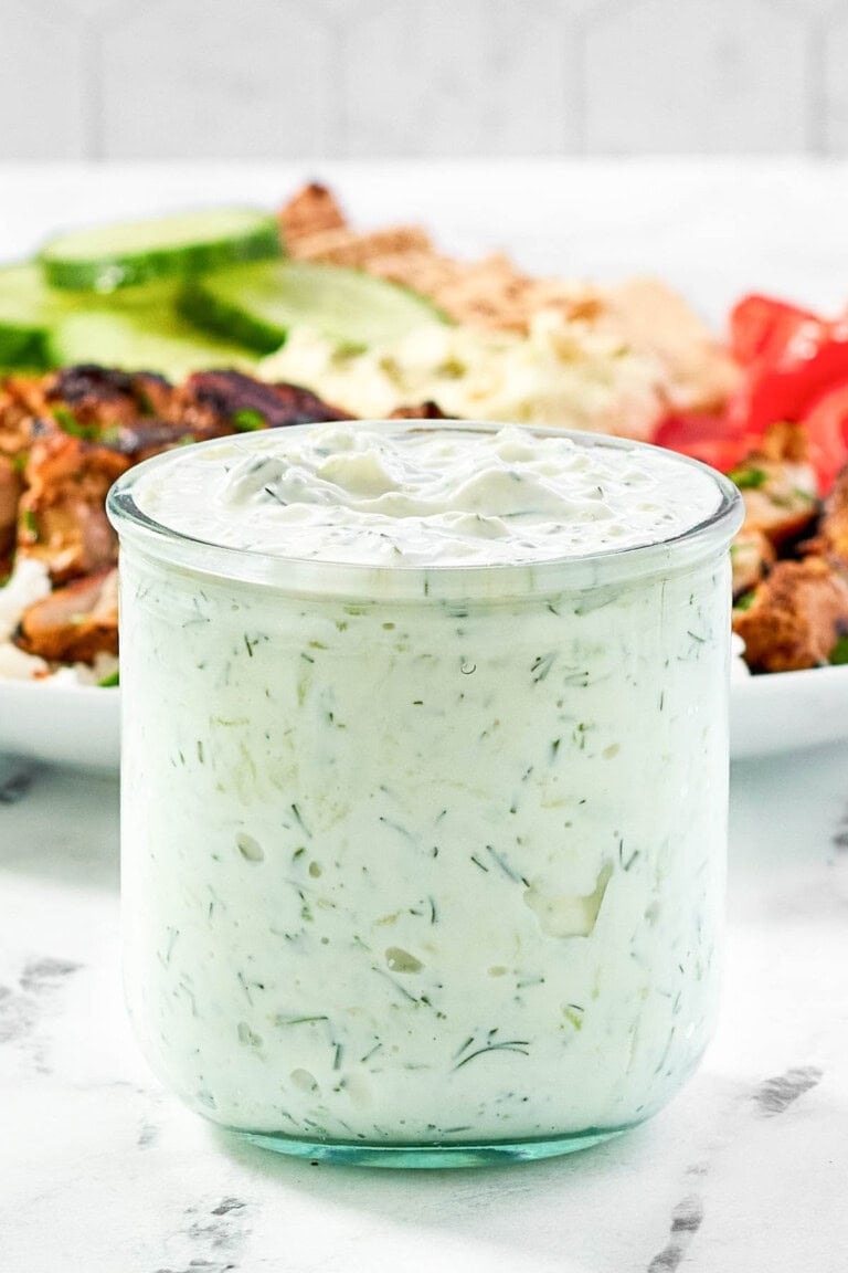 Creamy garlic dill yogurt sauce in a small jar in front of a salad.