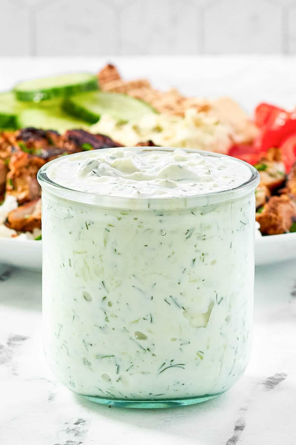 Creamy garlic dill yogurt sauce in a small jar in front of a salad.