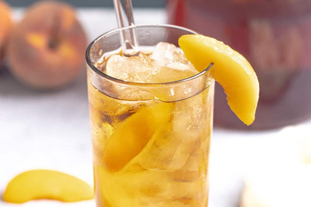 A glass of iced tea made with fresh peach syrup and garnished with a peach slice.