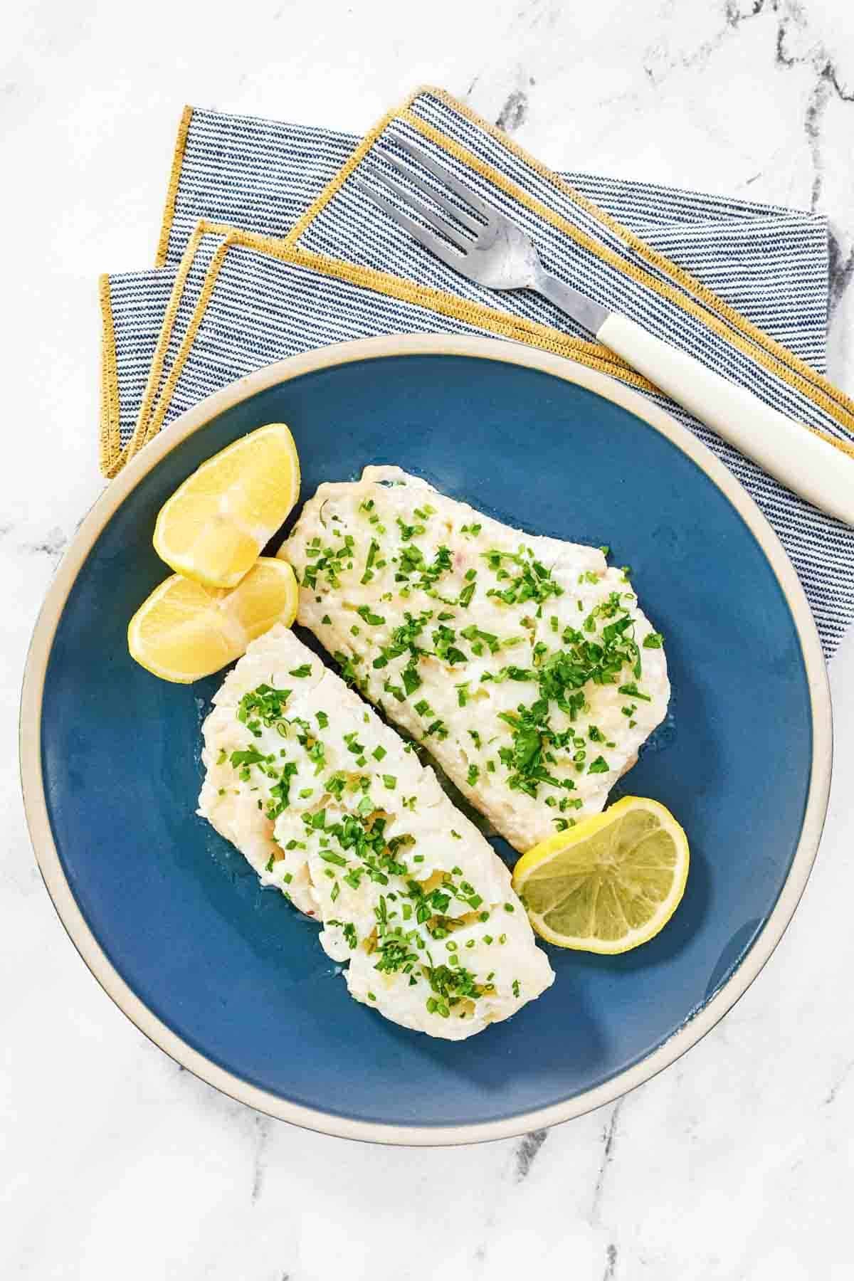 Lemon butter fish garnished with herbs and served with lemon wedges.